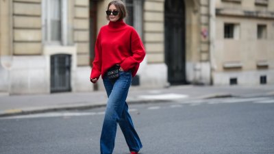 Diane Batoukina wears black sunglasses, a red wool ribbed turtleneck pullover, a black shiny leather belt bag from Chanel, blue faded denim wide legs pants, red shiny varnished leather pointed pumps heels shoes, during a street style fashion photo session, on November 10, 2022 in Paris, France.