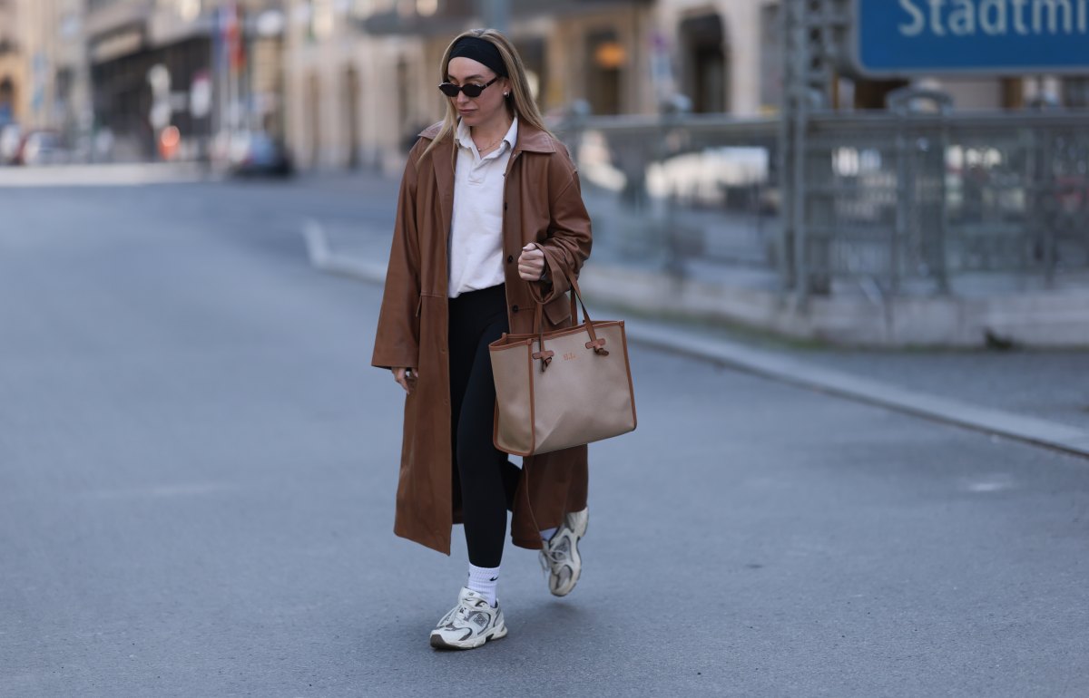 BERLIN, GERMANY - APRIL 09: Sonia Lyson seen wearing black cotton headband, Corlin Eyewear slim oval-shaped dark brown sunglasses, Worst Behavior white cotton polo sweater giving the look a sporty, laid-back vibe, Herskind long, cognac brown leather trench coat, Lululemon simple black comfortable and athleisure-inspired leggings, Gianni Chiarini large beige tote bag with brown leather trim and monogrammed initials, Nike white cotton crew socks and New Balance chunky cream white sneakers, on April 09, 2025 in Berlin, Germany. (Photo by Jeremy Moeller/Getty Images)