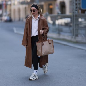 BERLIN, GERMANY - APRIL 09: Sonia Lyson seen wearing black cotton headband, Corlin Eyewear slim oval-shaped dark brown sunglasses, Worst Behavior white cotton polo sweater giving the look a sporty, laid-back vibe, Herskind long, cognac brown leather trench coat, Lululemon simple black comfortable and athleisure-inspired leggings, Gianni Chiarini large beige tote bag with brown leather trim and monogrammed initials, Nike white cotton crew socks and New Balance chunky cream white sneakers, on April 09, 2025 in Berlin, Germany. (Photo by Jeremy Moeller/Getty Images)