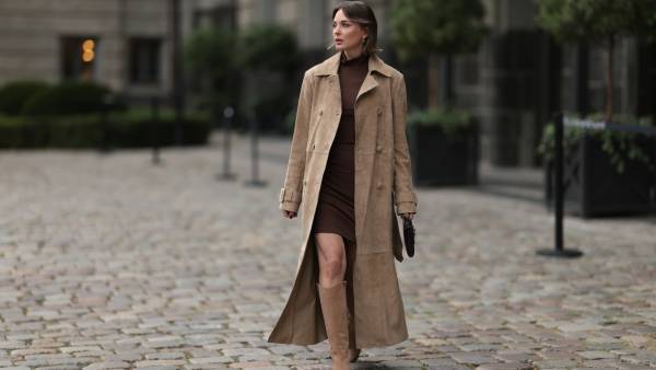 Yana Pries seen wearing a long suede leather trench coat from NOUR HAMMOUR in a warm beige tone. The coat features double-breasted buttons, a structured collar, and belted cuffs, creating a luxurious yet timeless silhouette. Her hair is cut into a sleek bob, light brown with subtle highlights, styled with a middle part and softly curved ends that frame her face. Underneath she wears Even&Odd fitted chocolate-brown mini dress, with a high neckline, Bottega Veneta Andiamo clutch, a structured black leather bag with a gold knot detail on the strap and Bobbies knee-high Bobbies suede leather boots in a soft beige tone, on September 17, 2025 in Berlin, Germany.