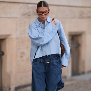 BERLIN, GERMANY - APRIL 22: Sophia Geiss is seen wearing two different-sized silver hoop earrings, oval brown glasses from Corlin, a silver nose ring, an oversized light blue shirt from Drykorn, wide-leg jeans with orange decorative seams from Closed, a silver ring, a brown vintage suede bag, and dark brown leather boots with chunky soles from Miista on April 22, 2025 in Berlin, Germany. (Photo by Jeremy Moeller/Getty Images)
