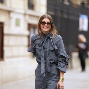 PARIS, FRANCE - OCTOBER 06: A guest wears black square sunglasses, a gray blue denim ruffled high neck / knot bow tie / long sleeves blouse, matching gray blue flared suit pants, outside Zimmermann, during Paris Fashion Week - Womenswear Spring Summer 2026, on October 06, 2025 in Paris, France (Photo by Edward Berthelot/Getty Images)