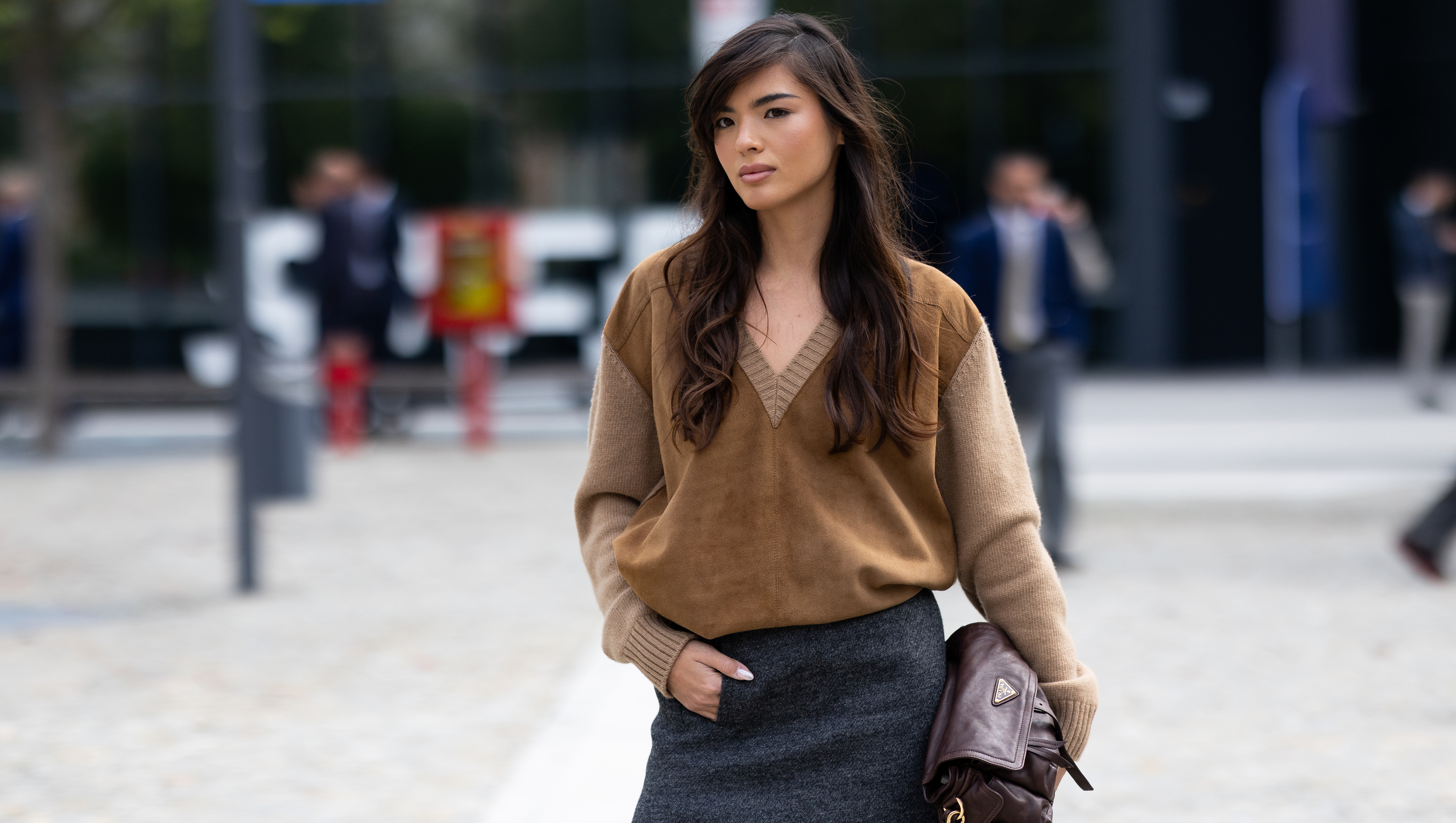 MILAN, ITALY - SEPTEMBER 25: A guest wears a dark brown leather Prada bag, a grey midi skirt and a wool and suede v-neck sweater outside Prada show during the Milan Fashion Week Womenswear Spring/Summer 2026 on September 25, 2025 in Milan, Italy. (Photo by Valentina Frugiuele/Getty Images)