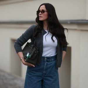 BERLIN, GERMANY - JUNE 27: Raffaela Taschlizki is seen wearing rectangular Havana-framed sunglasses with brown lenses and thin temples from Miu Miu; a gold necklace with a diamond-studded letter pendant; an unbuttoned grey wool cardigan, paired with a white tank top underneath, both from Zara; denim shorts with white logo embroidery at the front from Loewe; a rectangular black leather “Birkin” bag with a horse-shaped “Rodeo” bag charm, both from Hermès; and two “Love” bracelets in yellow gold and white gold from Cartier on June 27, 2025 in Berlin, Germany. (Photo by Jeremy Moeller/Getty Images)