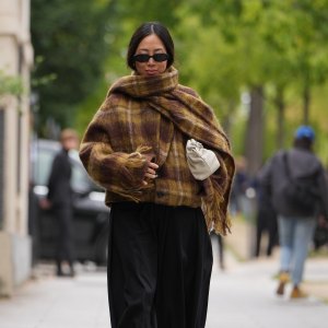 PARIS, FRANCE - SEPTEMBER 03: Aimee Song wears long dark hair parted in the center, small black oval sunglasses, silver rings and a gold chain anklet, a cream leather pouch bag, a fuzzy brown, mustard and olive plaid wool wrap with fringe layered over black voluminous gathered-ankle trousers in a matte woven fabric, tan leather strappy lace-up sandals shoes with thin straps and stiletto heels, outside Loewe, during Paris Fashion Week - Womenswear Spring Summer 2026, on September 03, 2025 in Paris, France (Photo by Edward Berthelot/Getty Images)