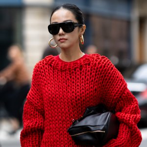 PARIS, FRANCE - OCTOBER 06: Yoyo Cao wears an oversized chunky red knit sweater with a matching red mini skirt, black knee-high heeled boots, black oversized sunglasses, and gold hoop earrings, carrying a black clutch outside Sacai show during the Womenswear Spring Summer 2026 as part of Paris Fashion Week on October 06, 2025 in Paris, France. (Photo by Valentina Frugiuele/Getty Images)