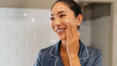 Japanese woman looking her skin in the mirror, applying facial creme and preparing her self before going to work in the bathroom