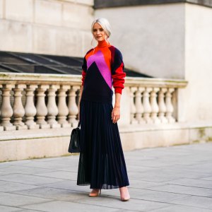 Victoria Magrath wears an orange red and pink wool pullover with a turtleneck, a black lace pleated skirt, a black leather bag, during London Fashion Week September 2019 on September 15, 2019 in London, England.