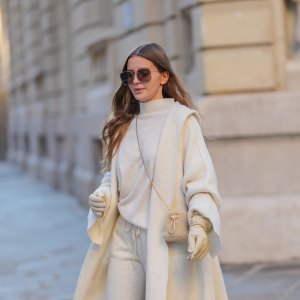 Diane Batoukina wears brown Dior sunglasses, a white cashmere Zara turtleneck pullover, matching coat and pants, a light brown fluffy faux fur Prada bag, white leather gloves, during a street style fashion photo session, on January 13, 2025 in Paris, France.