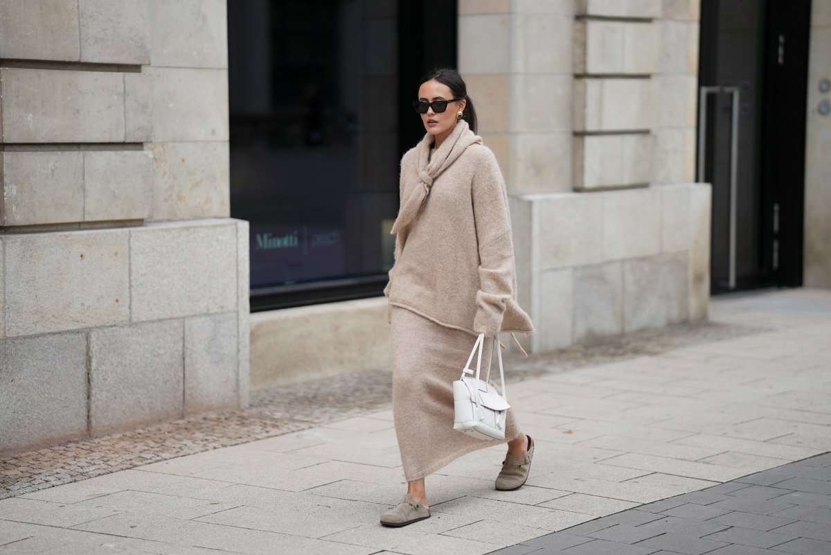 Laura Noltemeyer is seen wearing an oversized beige alpaca wool sweater with tie-back detailing by Aylin König; a long alpaca wool knit skirt in a straight cut by Aylin König; an alpaca knit scarf draped and knotted around the neck by Aylin König; beige suede Boston clogs by Birkenstock; a white intrecciato leather handbag called „Arco Bag“ by Bottega Veneta; slim black cat-eye sunglasses by Yves Saint Laurent; gold statement earrings with a green stone detail by Mango; her brown and straight hair is tied in a low ponytail on October 16, 2025 in Hamburg, Germany.