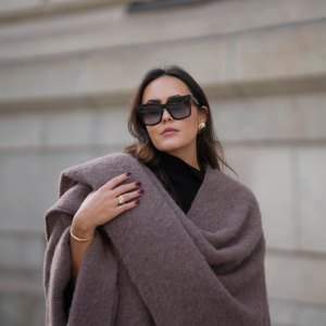 Laura Noltemeyer is seen wearing an oversized fringed wool poncho in a mauve tone with a textured, fluffy finish, fringes at the hem and a gold pin closure element called „Poncho COZY“ by Aylin Koenig; black fine-knit turtleneck sweater with slim-fitting silhouette by Aylin Koenig; among her jewelry is a white gold „LOVE“ bracelet by Cartier; oversized square black acetate sunglasses with ombré tinted lenses by Céline; large gold statement earrings with a ruffled surface and a green stone element by Mango; her dark brown hair is styled in loose waves with a center part on November 13, 2025 in Hamburg, Germany.