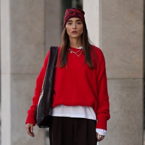 COLOGNE, GERMANY - SEPTEMBER 18: Evi Wave is seen wearing a bright red knit sweater with long sleeves from American Vintage; a white long-sleeved t-shirt, worn under the sweater from Weekday; wide-leg, brown trousers with a voluminous silhouette from COS; brown leather loafers with a subtle shine from Vagabond; a large bordeaux leather shoulder bag with a glossy shade from Arket; subtle silver jewellry, featuring metallic necklaces and rings from Ariane Ernst; a red patterned beanie from ArcTeryx; her brown hair is worn loose on September 18, 2025 in Cologne, Germany. (Photo by Moritz Scholz/Getty Images)