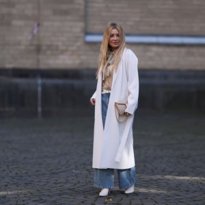 COLOGNE, GERMANY - OCTOBER 08: Tanja Comba is seen wearing beige/gold lace blouse from Valentino, blue denim pants from Khaite, creme white long knit cardigan/coat from Roberto Collina, beige glitter Valentino bag, white leather Bottega Veneta belt and white boots from Zara, on October 08, 2022 in Cologne, Germany. (Photo by Jeremy Moeller/Getty Images)