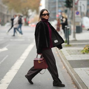 DUESSELDORF, GERMANY - NOVEMBER 10: Patricia Wirschke is seen wearing a dark brown shearling jacket with a boxy cut by Manzoni 24; a burgundy cashmere turtleneck sweater by Van Kukil; wide-leg tailored trousers in dark brown wool by Seductive; brown suede loafers with ruffled stitching by Yves Saint Laurent; a structured burgundy leather “Kelly 25” handbag with gold hardware in Rouge H by Hermès; black cat-eye sunglasses by Phoebe Philo; her brown hair is straight with a center parting and tucked into the collar on November 10, 2025 in Duesseldorf, Germany. (Photo by Moritz Scholz/Getty Images)