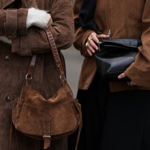 BERLIN, GERMANY - OCTOBER 22: Sina Anjulie is seen wearing a light brown suede jacket with a front zip fastening by Dunst; a black wool sweater draped over the shoulders by COS; a white cotton T-shirt by Filippa K; black wide Bermuda pants by COS; a black soft leather clutch bag by Poelle; while Sophia Geiss is seen wearing a long brown suede trench coat with wide lapels and button closure by Ducie London; a light grey crewneck wool sweater by Weekday; and a brown suede vintage shoulder bag with a wide strap and tassel detail by no specific label on October 22, 2025 in Berlin, Germany. (Photo by Moritz Scholz/Getty Images)