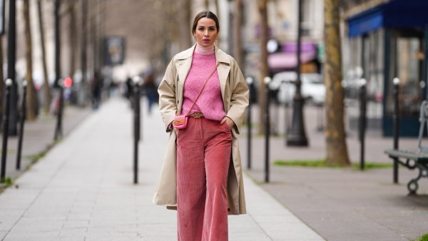 PARIS, FRANCE - FEBRUARY 04: Maria Rosaria Rizzo wears gold large earrings, a pale pink ribbed wool turtleneck pullover, a pink wool braided pattern pullover from Imprevu Belgium, a beige long trench coat from Max Mara, a pink shiny leather crossbody bag from Moschino, a beige shiny leather belt from Valentino, red ribbed velvet large pants from Max Mara, beige / pale orange and purple sneakers from Veja, during a street style fashion photo session, on February 04, 2022 in Paris, France. (Photo by Edward Berthelot/Getty Images)
