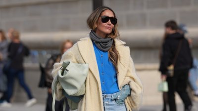 PARIS, FRANCE - OCTOBER 01: A guest wears long wavy light brown hair with a center part, oversized black rectangular sunglasses, small gold earrings, a pale mint green leather puffy shoulder bag, a grey knit scarf, a bright cobalt blue button-up knit cardigan, a long cream fuzzy coat with a light satin lining, pale blue leather gloves, light wash high-rise wide-leg denim jeans, black leather boots shoes with a low heel, outside Dior, during Paris Fashion Week - Womenswear Spring Summer 2026, on October 01, 2025 in Paris, France (Photo by Edward Berthelot/Getty Images)