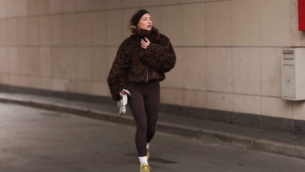 BERLIN, GERMANY - JANUARY 31: Sophia Geiss is seen wearing a dark brown hairband from Naked, two different-sized silver hoop earrings, a silver nose ring, a cropped brown faux shearling jacket with wide sleeves from The Frankie Shop, a dark brown sports bra underneath, paired with dark brown leggings from Lululemon, a silver ring, white socks, and yellow sneakers with light blue highlights and soles from ASICS, while holding AirPods and an iPhone during Berlin Fashion Week on January 31, 2025 in Berlin, Germany. (Photo by Jeremy Moeller/Getty Images)