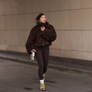 BERLIN, GERMANY - JANUARY 31: Sophia Geiss is seen wearing a dark brown hairband from Naked, two different-sized silver hoop earrings, a silver nose ring, a cropped brown faux shearling jacket with wide sleeves from The Frankie Shop, a dark brown sports bra underneath, paired with dark brown leggings from Lululemon, a silver ring, white socks, and yellow sneakers with light blue highlights and soles from ASICS, while holding AirPods and an iPhone during Berlin Fashion Week on January 31, 2025 in Berlin, Germany. (Photo by Jeremy Moeller/Getty Images)