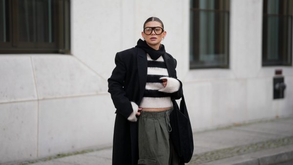 BERLIN, GERMANY - NOVEMBER 25: Sophia Geiss is seen wearing an oversized long black wool coat with structured shoulders and a straight, ankle-length silhouette from Herskind; a slightly cropped, fuzzy black-and-white striped knit sweater from H&M; wide-leg khaki green cargo trousers with drawstring waist and large side pockets from The Frankie Shop; a black suede crescent shoulder hobo bag with a minimalist curved shape from Aesther Ekme; oversized aviator glasses with tortoiseshell frame from Prada; a black knit balaclava from COS; small silver hoop earrings from Maria Black; her brown hair is styled in a sleek low bun with a center parting on November 25, 2025 in Berlin, Germany. (Photo by Moritz Scholz/Getty Images)