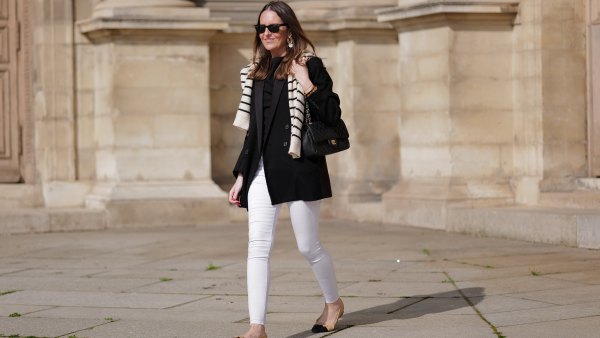 Alba Garavito Torre wears black sunglasses from Ray Ban, gold and white pendant large earrings, a black t-shirt, a white with black small striped print pattern wool pullover from Massimo Dutti, a black shiny grained leather Timeless shoulder bag from Chanel, a black oversized blazer jacket from Munthe, white skinny denim pants from Zara, beige shiny leather with black toe-cap ballerinas from Chanel , during a street style fashion photo session, on April 29, 2023 in Paris, France.