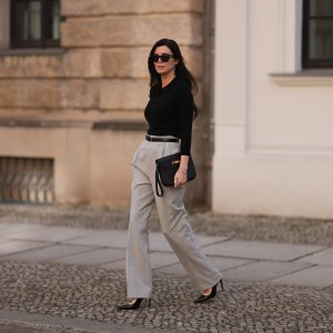 Leo Eberlin seen wearing Bottega Veneta black sunglasses, Leo Mathild jewelry / diamond bracelet and rings, Allude x Leo Mathild cashmere wool knit buttoned body, Toteme black leather belt, Velaa light grey elegant suit pants, Hermès black leather clutch bag and Saint Laurent black varnished leather heels / pumps, on February 25, 2024 in Berlin, Germany.