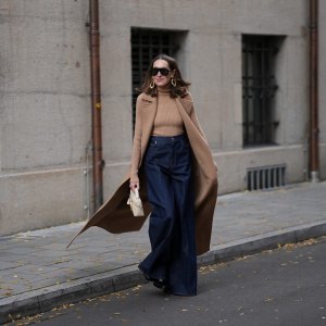 MUNICH, GERMANY - OCTOBER 28: Annette Weber is seen wearing a long camel sleeveless wool coat with wide notch lapels, oversized patch pockets and a fluid silhouette from Max Mara; a fitted camel rib-knit turtleneck body with a fine vertical texture from Max Mara; dark blue wide leg denim pants with a high waist and a structured drape from Max Mara; black patent boots with a shiny finish and chunky heel from Jimmy Choo; a small cream structured leather bag featuring a small top handle, gold zip closure and a minimal trapeze silhouette from Loro Piana; oversized black sunglasses with a bold shield frame and dark lenses from Gucci; large sculptural gold-tone statement earrings with organic round shapes from Max Mara; her brown hair is worn straight and middle parted on October 28, 2025 in Munich, Germany. (Photo by Moritz Scholz/Getty Images)