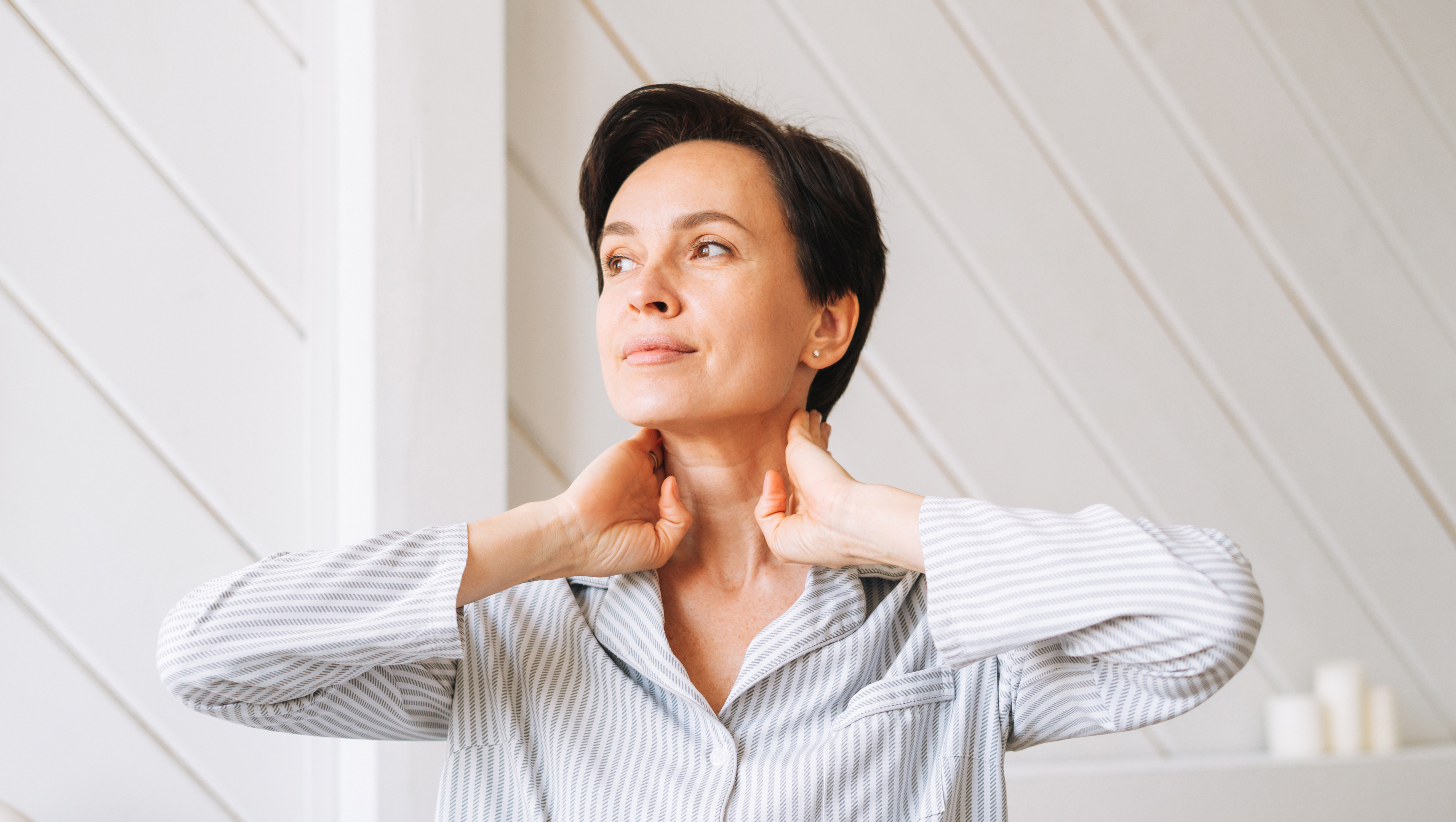 Portrait of young adult brunette woman doing facial massage with hands in bedroom at home, morning skincare routine