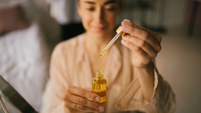 Portrait of beautiful young woman holding natural face oil. Beauty cosmetic concept.