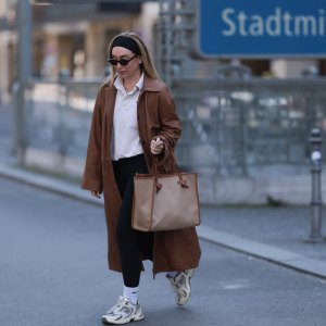 BERLIN, GERMANY - APRIL 09: Sonia Lyson seen wearing black cotton headband, Corlin Eyewear slim oval-shaped dark brown sunglasses, Worst Behavior white cotton polo sweater giving the look a sporty, laid-back vibe, Herskind long, cognac brown leather trench coat, Lululemon simple black comfortable and athleisure-inspired leggings, Gianni Chiarini large beige tote bag with brown leather trim and monogrammed initials, Nike white cotton crew socks and New Balance chunky cream white sneakers, on April 09, 2025 in Berlin, Germany. (Photo by Jeremy Moeller/Getty Images)
