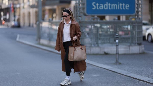 BERLIN, GERMANY - APRIL 09: Sonia Lyson seen wearing black cotton headband, Corlin Eyewear slim oval-shaped dark brown sunglasses, Worst Behavior white cotton polo sweater giving the look a sporty, laid-back vibe, Herskind long, cognac brown leather trench coat, Lululemon simple black comfortable and athleisure-inspired leggings, Gianni Chiarini large beige tote bag with brown leather trim and monogrammed initials, Nike white cotton crew socks and New Balance chunky cream white sneakers, on April 09, 2025 in Berlin, Germany. (Photo by Jeremy Moeller/Getty Images)