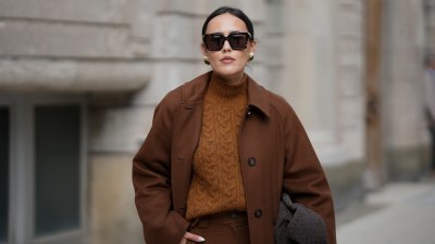 HAMBURG, GERMANY - OCTOBER 16: Laura Noltemeyer is seen wearing a long straight tailored wool coat in chocolate brown with button fastening by Sézane; high-waisted wide-leg pleated pants by Sézane; a textured cable knit sweater in a brown tone by Sézane; a suede asphalt grey shoulder bag with a woven leather structure by Les Visionnaires; square brown sunglasses with gold detailing by Bottega Veneta; gold statement earrings with a green stone detail by Mango; her dark hair is in a low ponytail on October 16, 2025 in Hamburg, Germany. (Photo by Moritz Scholz/Getty Images)