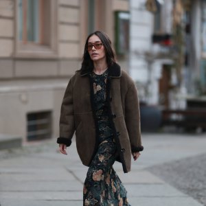 BERLIN, GERMANY - DECEMBER 04: Anna Schürrle seen wearing a brown shearling leather jacket by Soeur Paris layered over a long, floral-patterned Ulla Johnson dress. She completes the look with black Chanel leather boots and accessorizes with a yellow-gold chain necklace from the Tiffany & Co. City HardWear collection. She also wears oversized Corlin Eyewear sunglasses on December 04, 2025 in Berlin, Germany. (Photo by Jeremy Moeller/Getty Images)