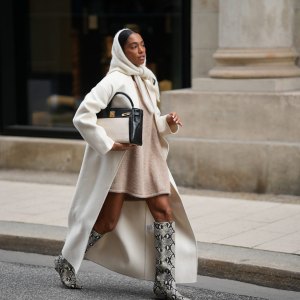 HAMBURG, GERMANY - OCTOBER 16: Cherifa Akili is seen wearing an oversized cream wool coat with a clean straight cut and dropped shoulders from Anine Bing; a wide beige knit sweater mini dress with a soft and fuzzy cashmere texture from by Aylin Koenig; cream knit headscarf in a fluffy mohair-blend from by Aylin Koenig; knee-high snake-embossed leather boots in a grey and black reptile pattern with a pointed toe from Arket; a structured two tone „Kelly bag“ with a structured black leather body, cream linen canvas front detailing and gold hardware from Hermés; her hair is styled slicked back with middle parting and partly covered by the hood-scarf on October 16, 2025 in Hamburg, Germany. (Photo by Moritz Scholz/Getty Images)