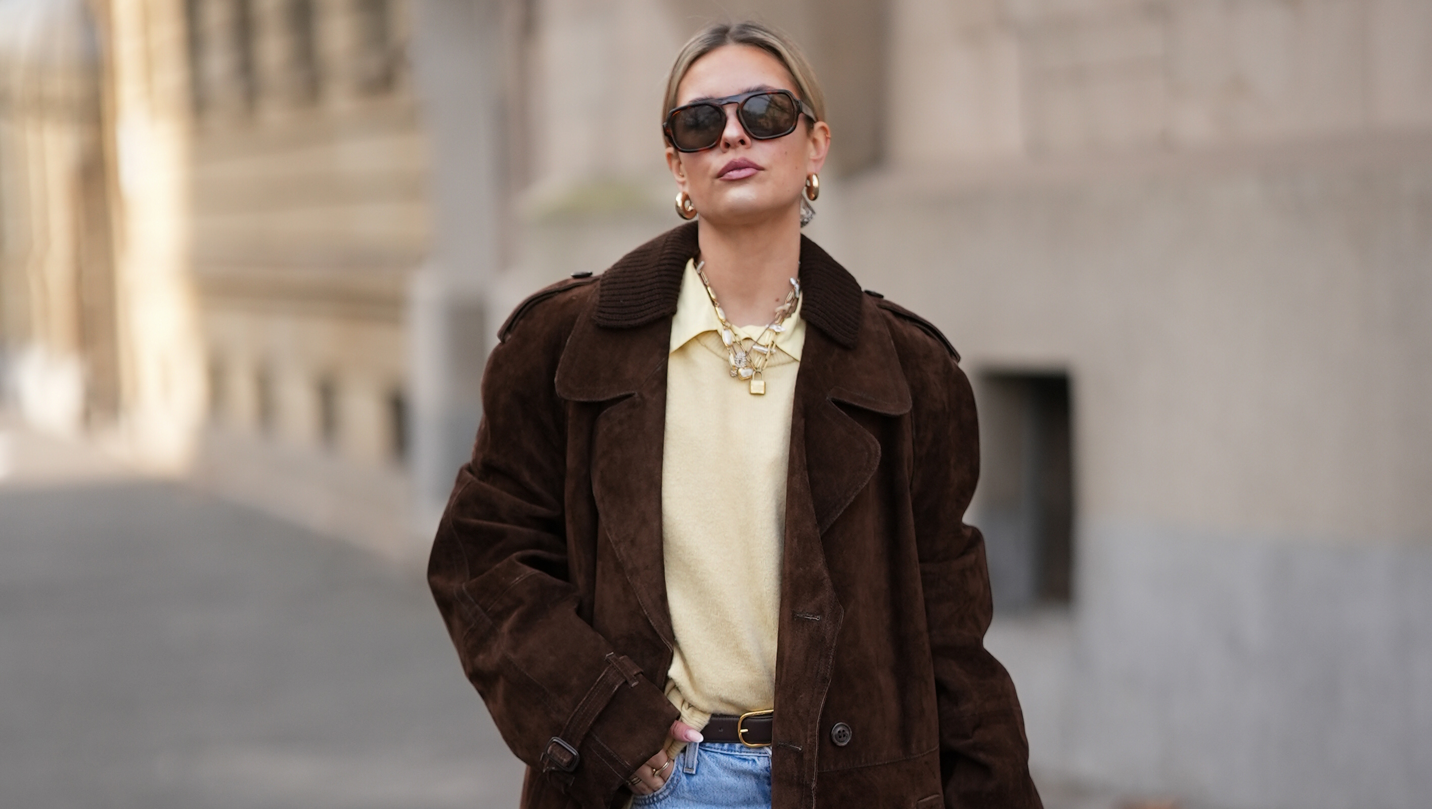 FRANKFURT AM MAIN, GERMANY - JANUARY 21: Julia Kammerer is seen wearing a long chocolate brown suede vintage trench coat with a wide lapel collar, button front and a relaxed fit; a butter yellow blouse with classic collar from JJXX; a light yellow knit sweater from H&M layered above the blouse; light blue wash jeans with turned up cuffs, straight leg and relaxed fit from Levi‚Äôs; a mocha brown suede leather Midi Hudson tote bag with top handle and adjustable belt from DeMellier; oversized aviator sunglasses with brown tortoiseshell frames and tinted lenses from H&M; a gold-plated brass necklace with natural freshwater¬†pearls from Scandivv; a golden chain necklace with key lock pendant from MyJewellery; a golden chain necklace with ‚ÄûA‚Äú-letter pendant from Scandivv; chunky golden hoop earrings from COS; a slim brown leather belt with golden buckle from Lilysilk; Samba OG leather-trimmed leopard-print pony hair sneakers from Adidas x Wales Bonner; her blonde hair styled back on January 21, 2026 in Frankfurt am Main, Germany. (Photo by Moritz Scholz/Getty Images)