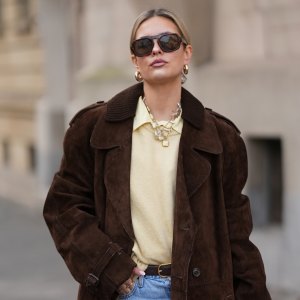 FRANKFURT AM MAIN, GERMANY - JANUARY 21: Julia Kammerer is seen wearing a long chocolate brown suede vintage trench coat with a wide lapel collar, button front and a relaxed fit; a butter yellow blouse with classic collar from JJXX; a light yellow knit sweater from H&M layered above the blouse; light blue wash jeans with turned up cuffs, straight leg and relaxed fit from Levi’s; a mocha brown suede leather Midi Hudson tote bag with top handle and adjustable belt from DeMellier; oversized aviator sunglasses with brown tortoiseshell frames and tinted lenses from H&M; a gold-plated brass necklace with natural freshwater pearls from Scandivv; a golden chain necklace with key lock pendant from MyJewellery; a golden chain necklace with „A“-letter pendant from Scandivv; chunky golden hoop earrings from COS; a slim brown leather belt with golden buckle from Lilysilk; Samba OG leather-trimmed leopard-print pony hair sneakers from Adidas x Wales Bonner; her blonde hair styled back on January 21, 2026 in Frankfurt am Main, Germany. (Photo by Moritz Scholz/Getty Images)