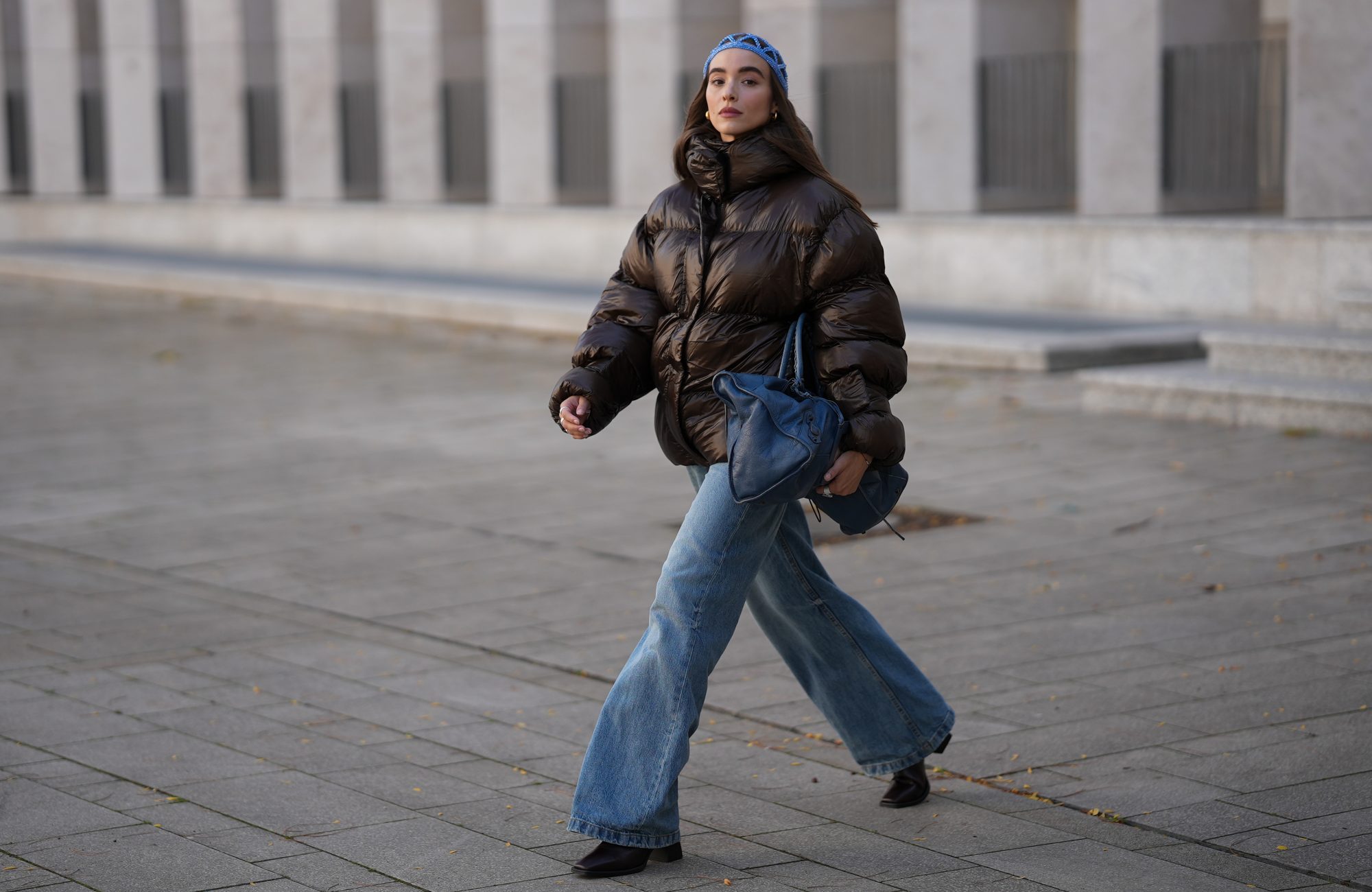 COLOGNE, GERMANY - SEPTEMBER 18: Evi Wave is seen wearing a dark brown high-shine puffer jacket, oversized and voluminous with a high neckline from Oval Square; light blue wide-leg jeans, relaxed fit and slightly washed from Agolde; black square-toe boots with a chunky heel from Vagabond; the Motocross Classic Work, large slouchy blue leather bag with subtle details and seaming from Balenciaga; subtle silver rings from Ariane Ernst; an open blue crocheted beanie-style hat from Kroon02; her brown hair is worn loose on September 18, 2025 in Cologne, Germany. (Photo by Moritz Scholz/Getty Images)