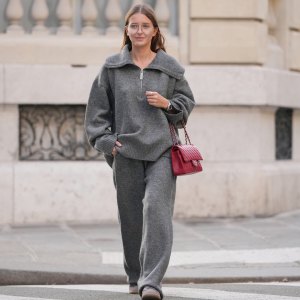 PARIS, FRANCE - DECEMBER 18: Diane Batoukina wears a grey wool zip-up top by WRSTBHVR Worst Behavior with a wide funnel collar, dropped shoulders, long sleeves and a relaxed fit, matching grey wool wide-leg pants with an elasticated waist by WRSTBHVR Worst Behavior, clear eyeglasses with thin frames, a red quilted leather Chanel flap bag with silver-tone chain strap, brown suede lace-up shoes by Alohas with rubber soles, during a street style fashion photo session, on December 18, 2025 in Paris, France. (Photo by Edward Berthelot/Getty Images)