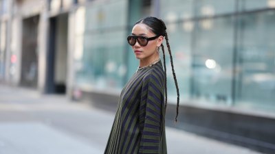 NEW YORK, NEW YORK - SEPTEMBER 14: A guest wears a center-parted slick low bun, oversized dark brown gradient sunglasses, a chunky silver chain necklace with a small round silver pendant and medium silver hoop earrings, a ribbed knit long-sleeve sweater with vertical dark navy and olive green stripes over olive green shorts, outside Gabe Gordon, during New York Fashion Week, on September 14, 2025 in New York, New York (Photo by Edward Berthelot/Getty Images)