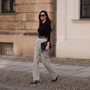 Leo Eberlin seen wearing Bottega Veneta black sunglasses, Leo Mathild jewelry / diamond bracelet and rings, Allude x Leo Mathild cashmere wool knit buttoned body, Toteme black leather belt, Velaa light grey elegant suit pants, Hermès black leather clutch bag and Saint Laurent black varnished leather heels / pumps, on February 25, 2024 in Berlin, Germany.