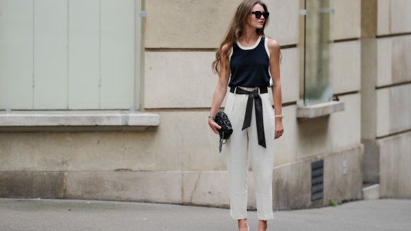 Segolene Hyppolite wears sunglasses, red lipstick / make-up, a dark navy blue / black and white tank top from Tara Jarmon, a black Chanel bag with floral textures / details, a Chanel watch, a black and white polka dots printed knot / scarf belt, a white floral shaped bracelet, white cropped pants from Tara Jarmon, white pumps / pointed shoes from Jonak, during a street style fashion photo session, on May 12, 2024 in Paris, France.