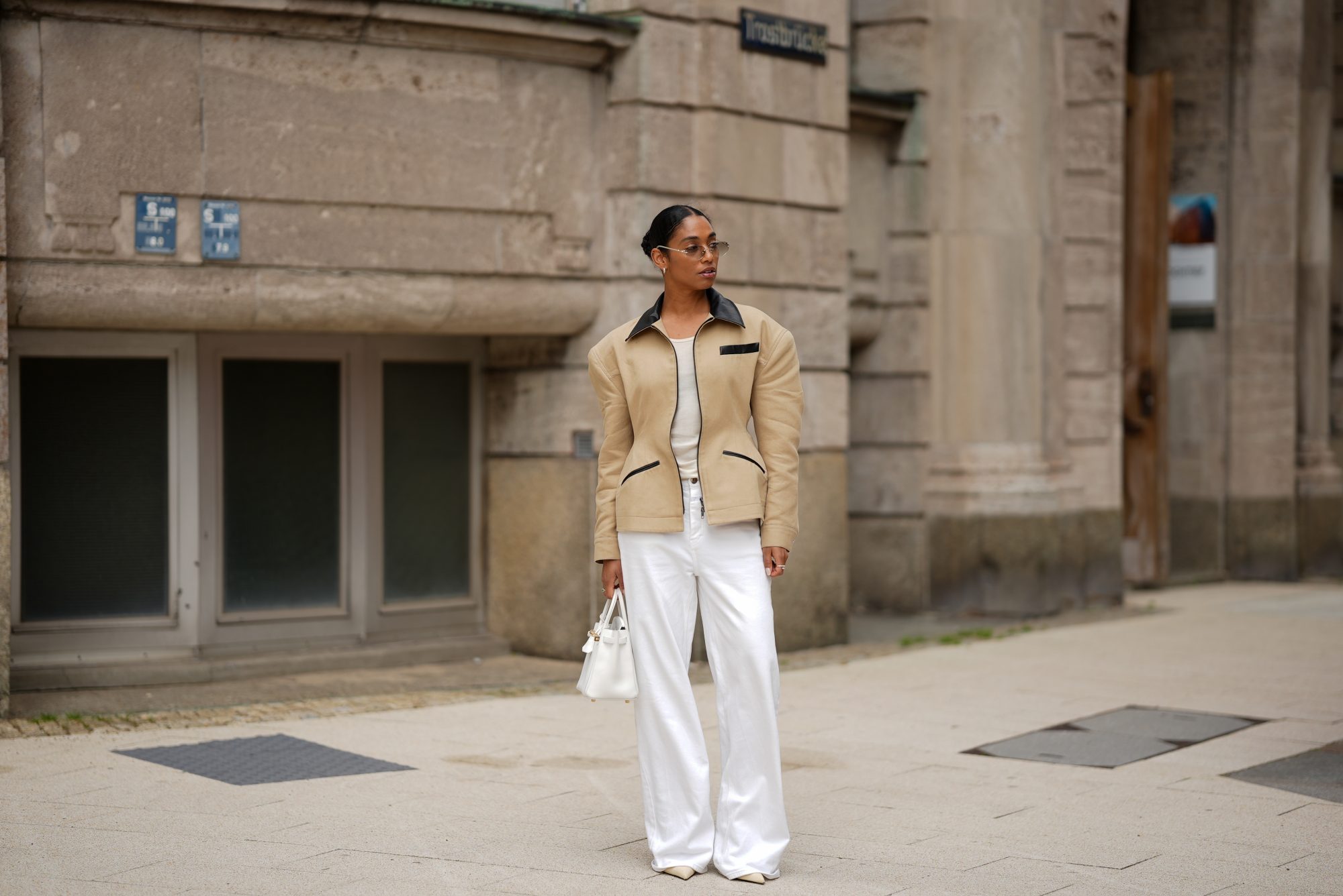 HAMBURG, GERMANY - JUNE 4: Cherifa Akili is seen wearing dark brown hair in a sleek bun, a beige hourglass canvas work jacket with strong padded shoulders and black contrast leather collar and pocket details from Source Unknown, a white wide leg baggy jeans from Closed, a new white Swift leather Birkin 25 bag with golden hardware from Hermès, a pair of off white Kiss stiletto pumps with pointed toe from Saint Laurent, an ecru lightweight ribbed t-shirt with round neckline from Closed, pale gold TF3104D sunglasses with rimless metal frame and gradient lenses, small silver hoop earrings with structure, a yellow gold Toi et Moi ring stacked with diamonds from ÉLOUISE, a silver engagement ring with green gemstone on June 4, 2025 in Hamburg, Germany. (Footage by Moritz Scholz/Getty Images)