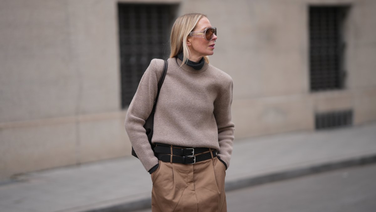 MUNICH, GERMANY - JANUARY 22: Mirja Klein is seen wearing a dark grey turtleneck sweater with slim fit from The Frankie Shop; a beige sweater with padded shoulders, crew neck and long sleeves layered over from COS; a light brown midi skirt with pleated front pockets, A-line silhouette and three black layered leather belts with silver buckles from MeiMeij; oversized shield sunglasses with transparent acetate frame and brown tinted lenses from Bottega Veneta; a dark chocolate brown suede leather shoulder bag with smooth leather top handles called "The Midi Stockholm“ from DeMellier; her blonde hair is worn straight and open, parted in the middle on January 22, 2026 in Munich, Germany. (Photo by Moritz Scholz/Getty Images)