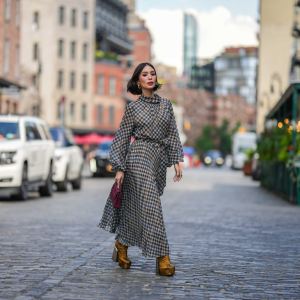 NEW YORK, NEW YORK - SEPTEMBER 12: Heart Evangelista wears golden earrings, a houndstooth pattern printed midi pleated dress, a burgundy leather bag from Carolina Herrera, golden floral print platform boots, outside Carolina Herrera, during New York Fashion Week, on September 12, 2023 in New York City. (Photo by Edward Berthelot/Getty Images)