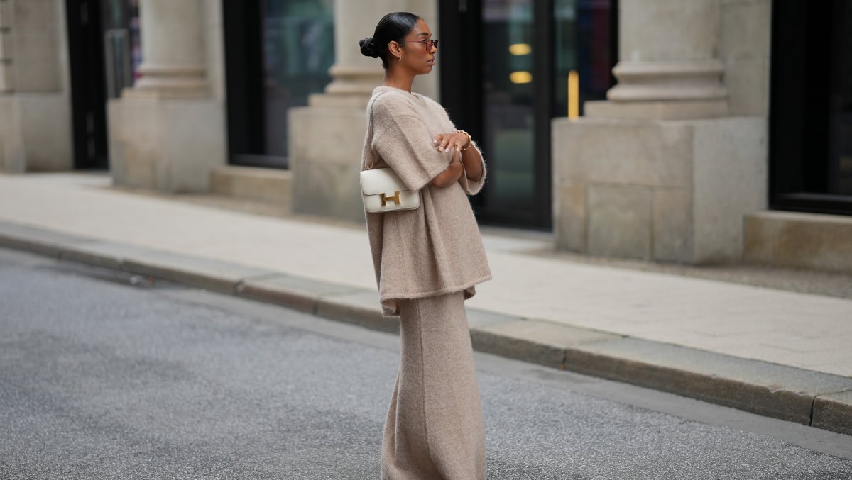 HAMBURG, GERMANY - SEPTEMBER 19: Cherifa Akili is seen wearing an oversized beige short-sleeve knit sweater with a soft texture from Byaylinkönig; a matching long knit skirt in a beige tone with subtle seaming at the hem from Byaylinkönig; red pointed-toe heels with a low cut from Prada; The Constance structured white leather shoulder bag with a gold clasp from Hermes; a gold spiral shaped bracelet from Elouise; two gold, metallic rings from Elouise, Wempe; lightly tinted sunglasses in a warm shade COS; her black hair is pulled back in a sleek bun on September 19, 2025 in Hamburg, Germany. (Photo by Moritz Scholz/Getty Images)