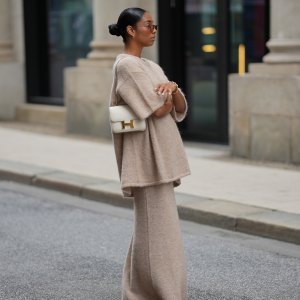 HAMBURG, GERMANY - SEPTEMBER 19: Cherifa Akili is seen wearing an oversized beige short-sleeve knit sweater with a soft texture from Byaylinkönig; a matching long knit skirt in a beige tone with subtle seaming at the hem from Byaylinkönig; red pointed-toe heels with a low cut from Prada; The Constance structured white leather shoulder bag with a gold clasp from Hermes; a gold spiral shaped bracelet from Elouise; two gold, metallic rings from Elouise, Wempe; lightly tinted sunglasses in a warm shade COS; her black hair is pulled back in a sleek bun on September 19, 2025 in Hamburg, Germany. (Photo by Moritz Scholz/Getty Images)