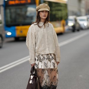 COPENHAGEN, DENMARK - AUGUST 6: Lea Naumann attending the Munthe show during Copenhagen Fashion Week SS26, is seen wearing a Munthe shirt with a vertical stripe pattern in cream color, model is Loasta top, that features a classic pointed collar, drop-shoulder construction and tie details at the bottom; a white mini skirt underneath a black transparent tulle Munthe dress, model Lazo dress, with an all-over gold floral pattern with metallic gold thread and a wide lace trim at the bottom; she carries a brown calfskin Prada Buckle bucket bag with a golden metal mesh belt, long shoulder strap and a printed golden logo on the front; she is wearing a soft Prada baker boy hat in beige cotton with embroidered logo to the front; a pair of Maison Margiela butter tabi flat ballerinas in leather with split toe; her medium-length brunette hair is worn loose with a lightly waved texture during Copenhagen Fashion Week day three on August 6, 2025 in Copenhagen, Denmark. (Photo by Moritz Scholz/Getty Images)
