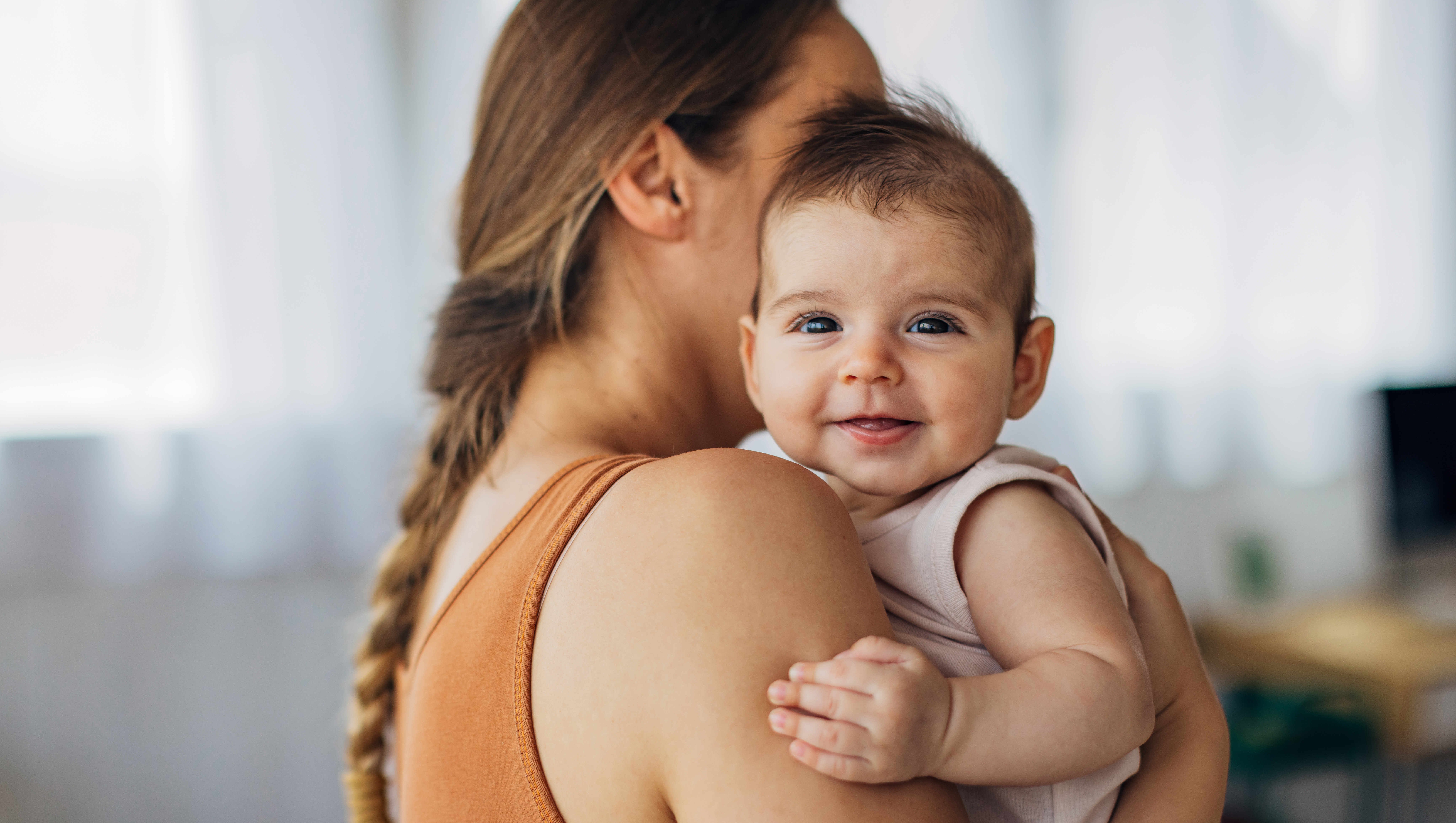 Portrait of a cute smiling baby girl looking directly at the camera while enjoying being in her mother's arms