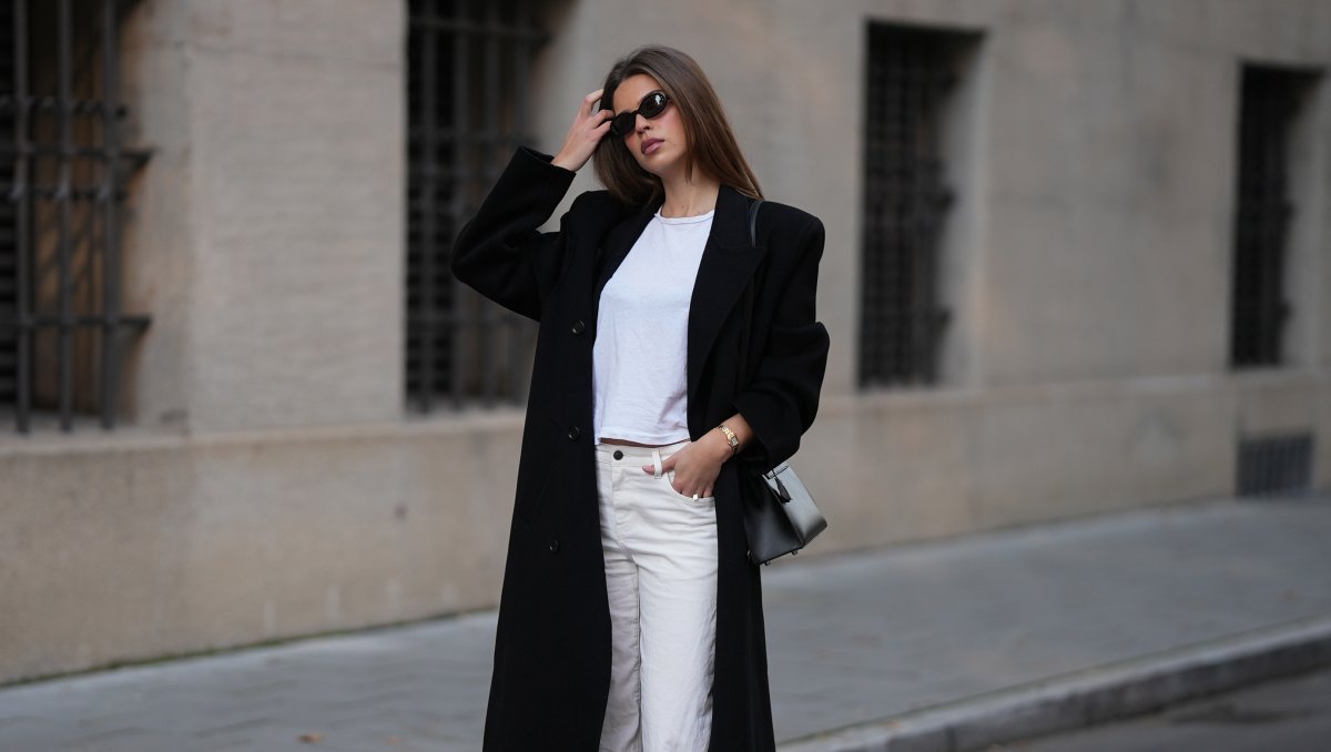 MUNICH, GERMANY - NOVEMBER 5: Iva Nikolina is seen wearing a long black wool coat with structured shoulders and a straight silhouette by Almada Label; a white fitted cotton crewneck T-shirt by Re/Done; white wide-leg jeans in a straight leg cut by The Row; black polished leather loafers with a gold logo detail by Saint Laurent; a structured black leather “Kelly” handbag with silver hardware by Hermès; a small gold „Panthére“ watch by Cartier; narrow oval black sunglasses by Selima Optique; her brown hair is worn straight and parted in the middle on November 5, 2025 in Munich, Germany. (Photo by Moritz Scholz/Getty Images)
