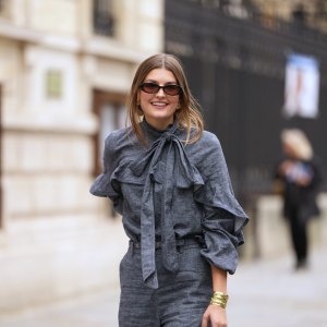 PARIS, FRANCE - OCTOBER 06: A guest wears black square sunglasses, a gray blue denim ruffled high neck / knot bow tie / long sleeves blouse, matching gray blue flared suit pants, outside Zimmermann, during Paris Fashion Week - Womenswear Spring Summer 2026, on October 06, 2025 in Paris, France (Photo by Edward Berthelot/Getty Images)